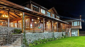 Une grande maison en bois à plusieurs étages, avec des fondations en pierre, un porche abrité et une pelouse bien entretenue.