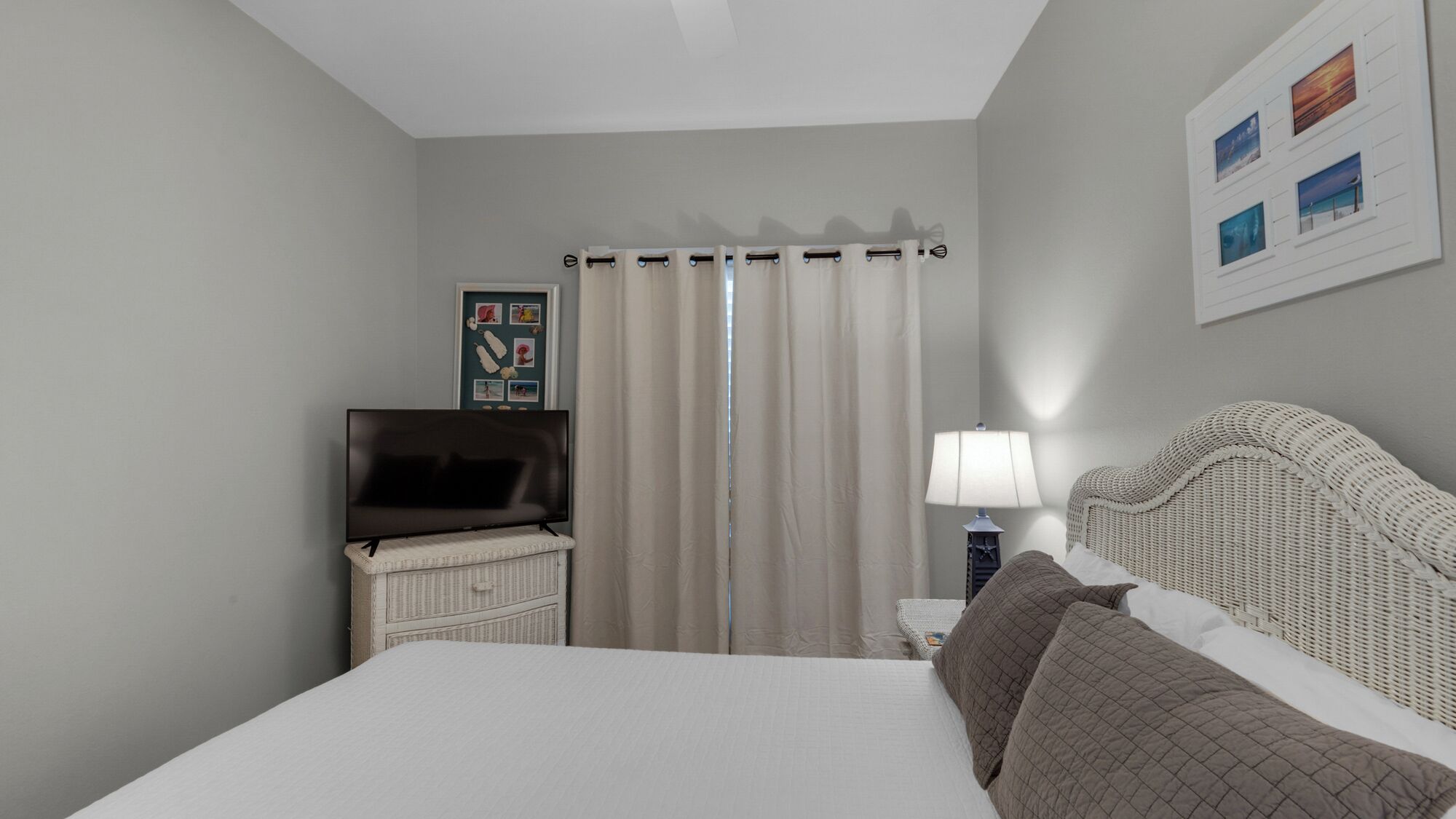 Une chambre d’hôtel avec un lit, une télévision, une lampe, une tête de lit en osier et un rideau.