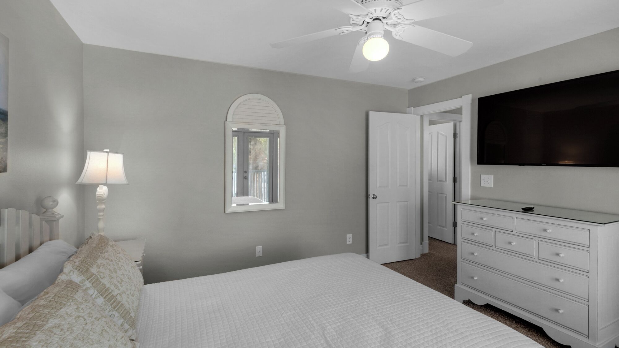 Un dormitorio con cama, cómoda, televisión y ventilador de techo.