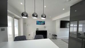 Un espace de salle à manger moderne avec une table blanche, trois suspensions et une cheminée.