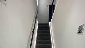 Un escalier recouvert d’une moquette noire, avec un paillasson au bas.
