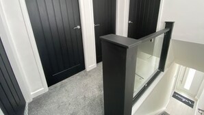 Un couloir avec trois portes en bois sombre, une rambarde en verre et un sol recouvert de moquette.