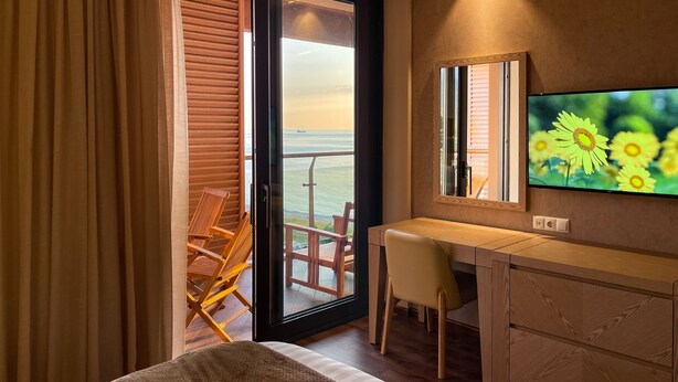 Une chambre d’hôtel équipée d’un lit, d’un bureau, d’une chaise, d’une télévision et offrant une vue sur la mer grâce à une porte coulissante.