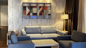 Un salon moderne comprenant un canapé d’angle, deux fauteuils, une table basse en verre et un téléviseur fixé au mur.