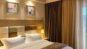 Une chambre d’hôtel avec un grand lit, une tête de lit, deux tables de chevet, une lampe et une fenêtre avec des rideaux.