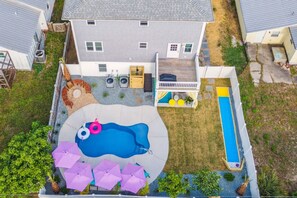 A residential backyard with a swimming pool, a deck, and a small patio area.