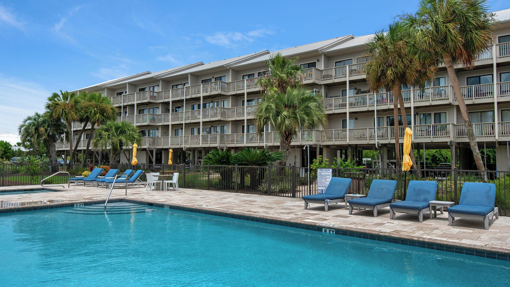 A hotel with a swimming pool, lounge chairs, and palm trees.