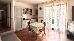 Een kleine keuken met witte kastjes, een eettafel met stoelen en een televisie.