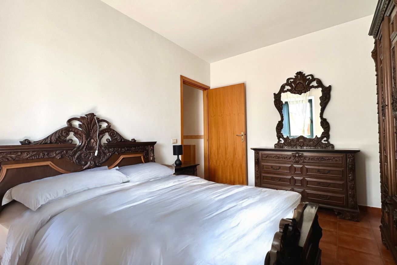 Een slaapkamer met een groot bed, een houten dressoir en een spiegel.
