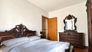 Een slaapkamer met een groot bed, een houten dressoir en een spiegel.