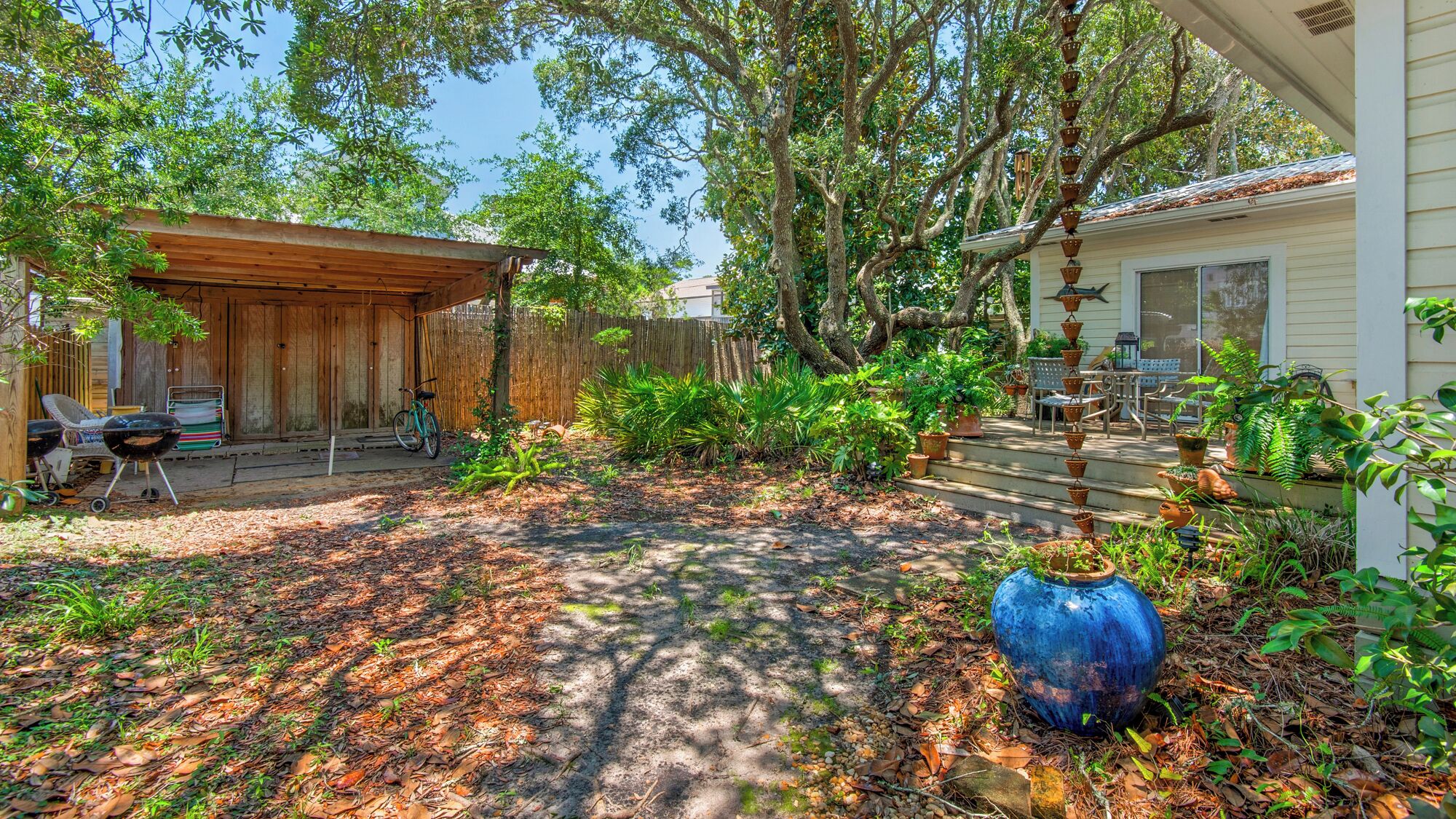 Um quintal com pérgola de madeira, churrasqueira e diversos vasos de plantas.