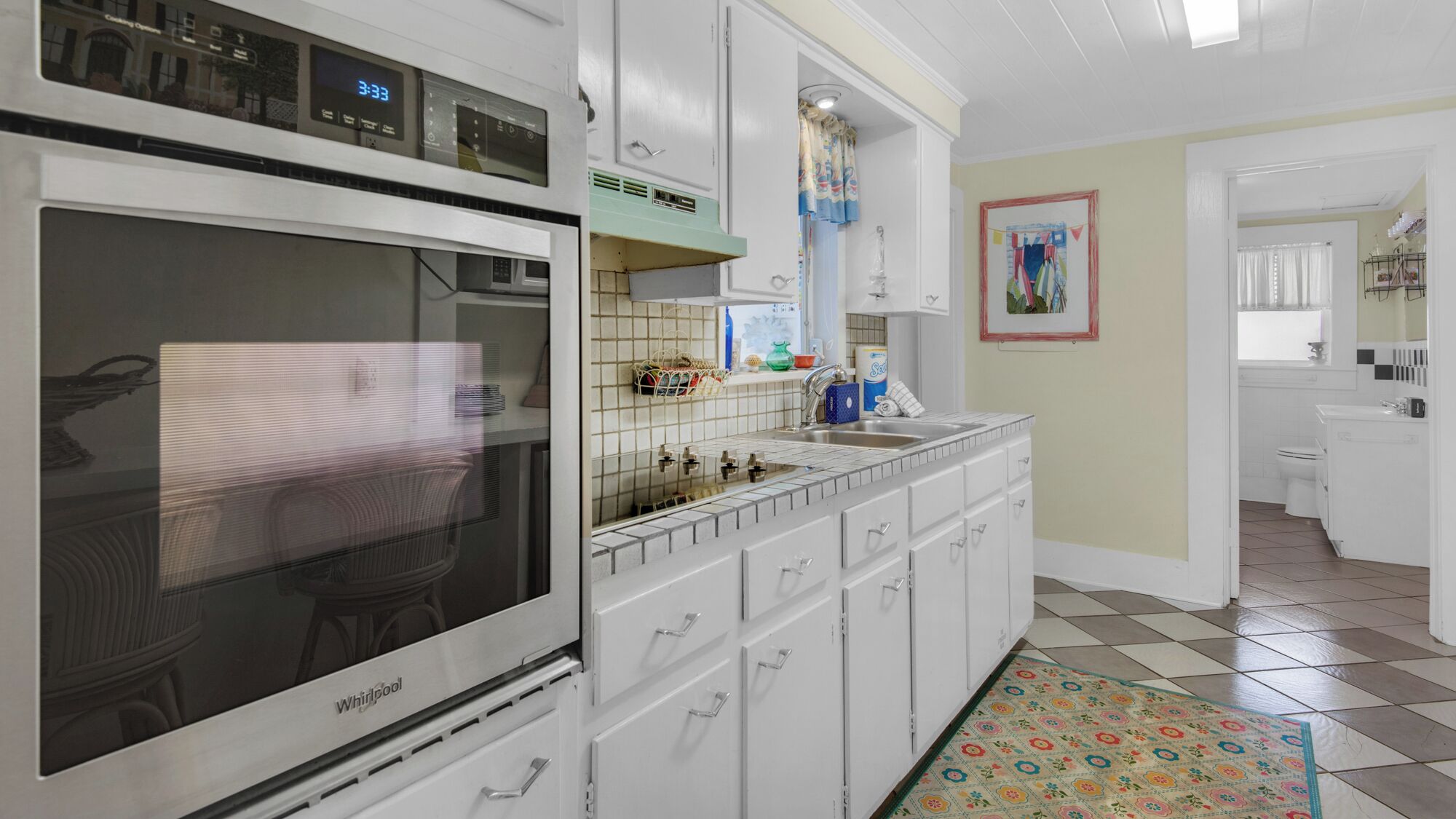 A kitchen with a Whirlpool oven, white cabinets, a tiled backsplash, and a colorful rug.
