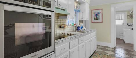 A kitchen with a Whirlpool oven, white cabinets, a tiled backsplash, and a colorful rug.