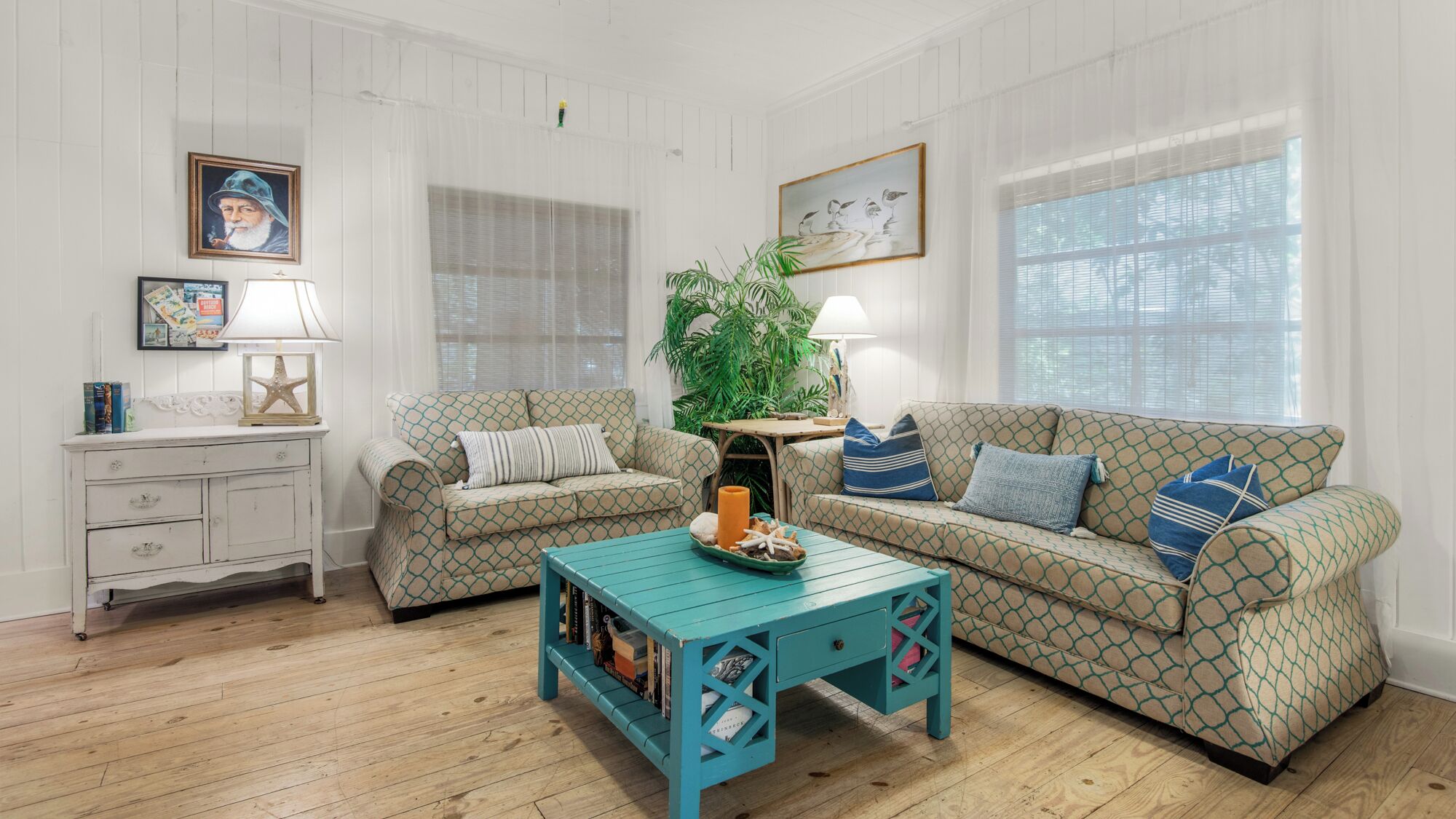 Una sala de estar acogedora con dos sofás estampados, una mesa de centro color aguamarina y un aparador blanco.