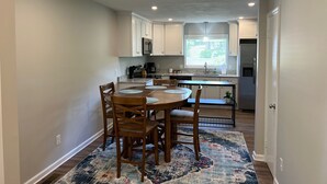 A modern kitchen with white cabinets, a stainless steel refrigerator, and a dining area with a wooden table and chairs. - Cute McRee Manor with large screened porch (Valdosta)
