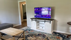 A living room with a flat-screen TV on a white cabinet, a grey couch, a wooden coffee table, and a patterned rug. - Cute McRee Manor with large screened porch (Valdosta)