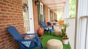 Une véranda couverte avec des murs en briques, des fauteuils Adirondack bleus et une petite table agrémentée de plantes en pot.