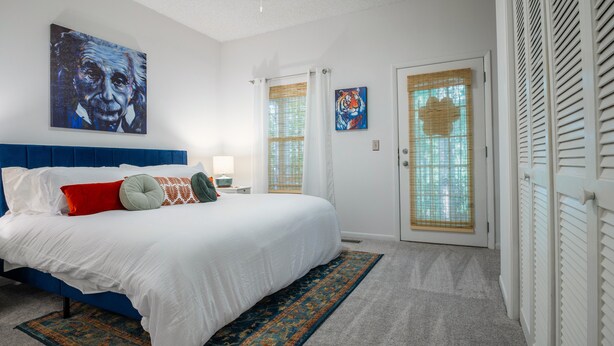 Une chambre à coucher avec un grand lit, une tête de lit bleue, un tapis à motifs et des œuvres d’art accrochées aux murs.