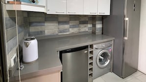 Een kleine keuken met witte kastjes, een roestvrijstalen koelkast, een inbouw vaatwasser en een wasmachine.