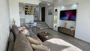 Een moderne woonkamer met een bank, salontafel en televisie. Een trap leidt naar een verdieping.
