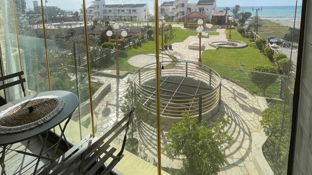 Een balkon met uitzicht op een aangelegde tuin, inclusief een ronde constructie en een strand.