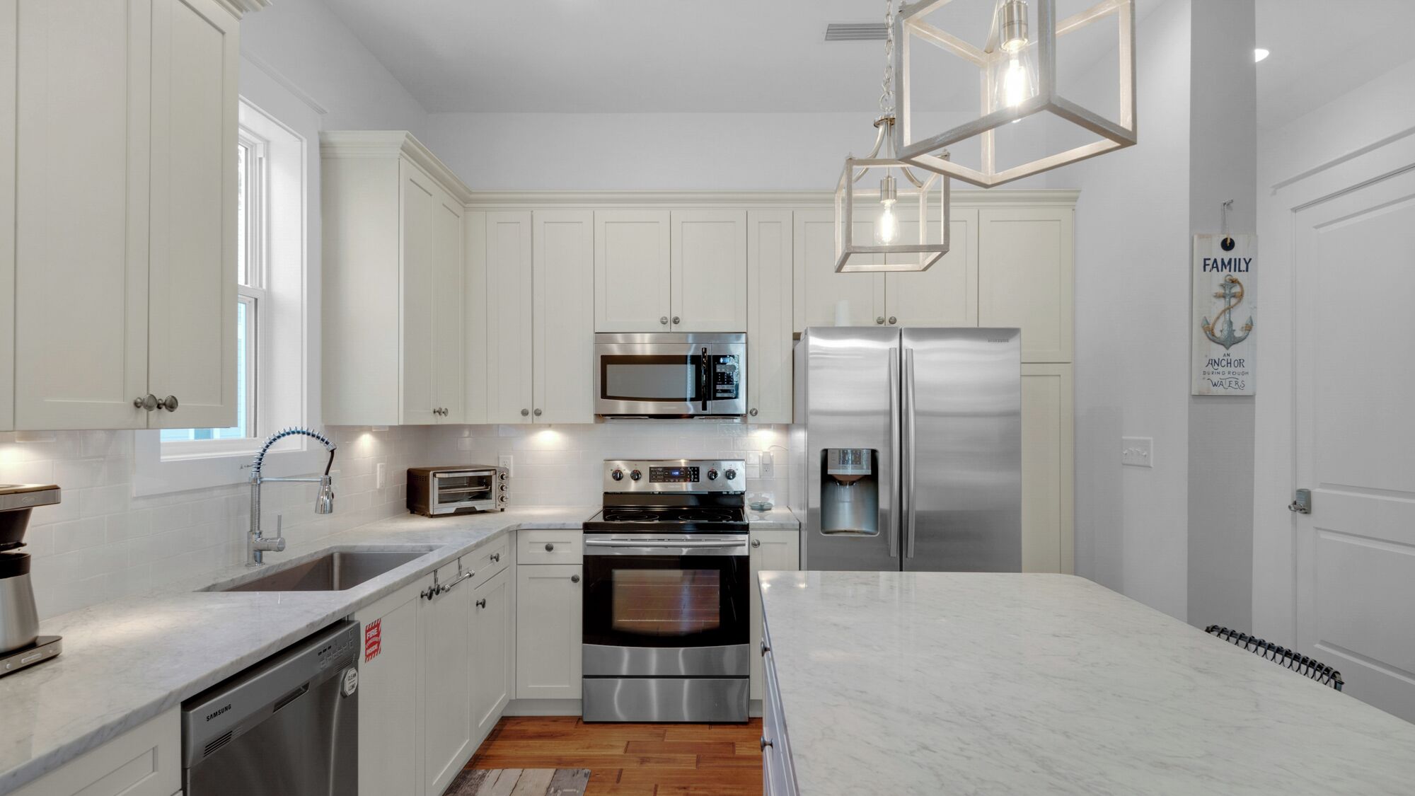 A modern kitchen with white cabinetry, stainless steel appliances, and a marble countertop.