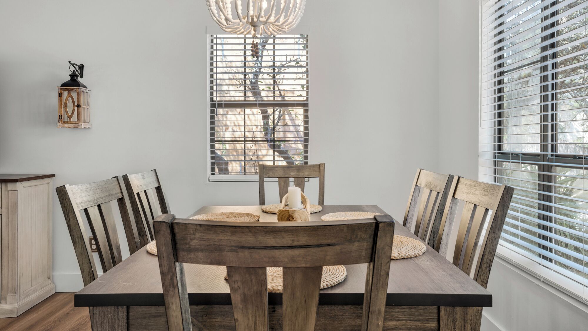 Comedor con mesa y sillas de madera, candelabro, ventana con persianas y una lámpara de pared.