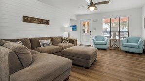 A living room with a sectional sofa, two armchairs, a ceiling fan, and a wooden floor.