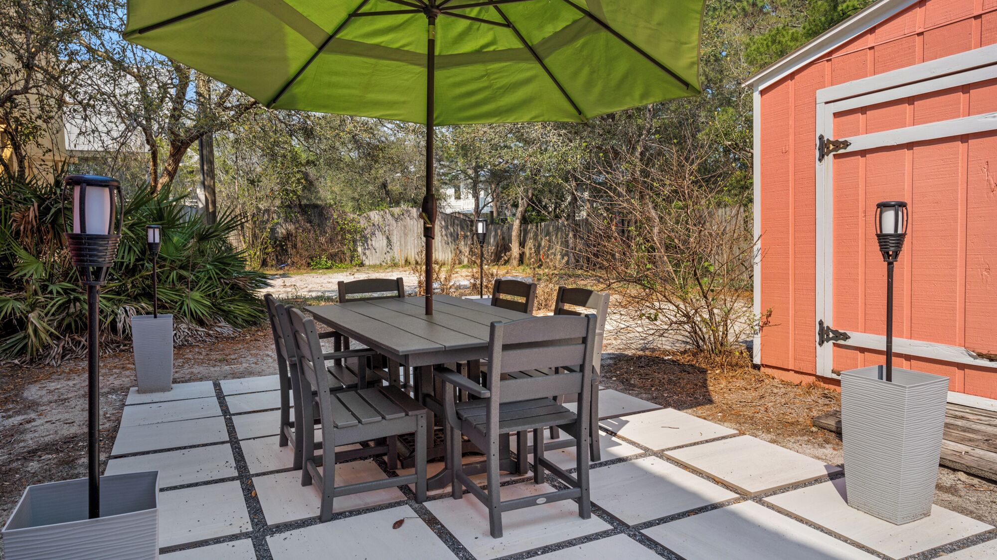 An outdoor patio with a table and chairs, a green umbrella, and a red shed in the background.