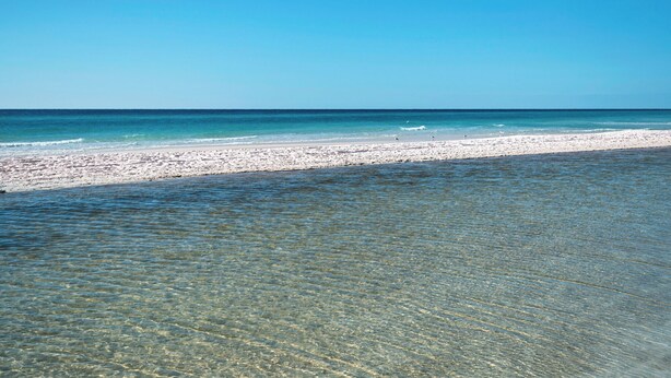 A beach with clear shallow waters leading to a sandy shore.
