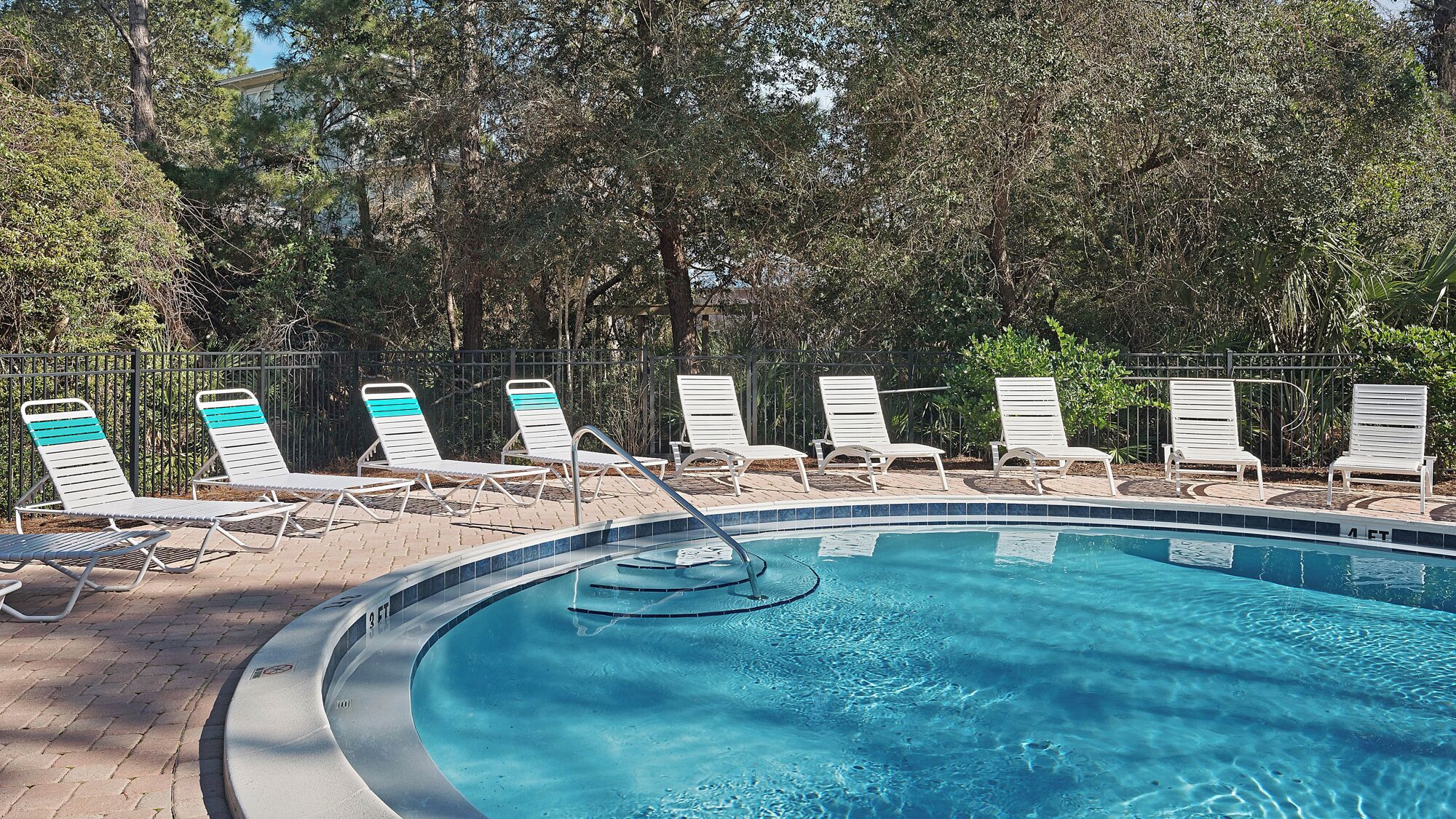 A swimming pool with white lounge chairs and a tiled edge.
