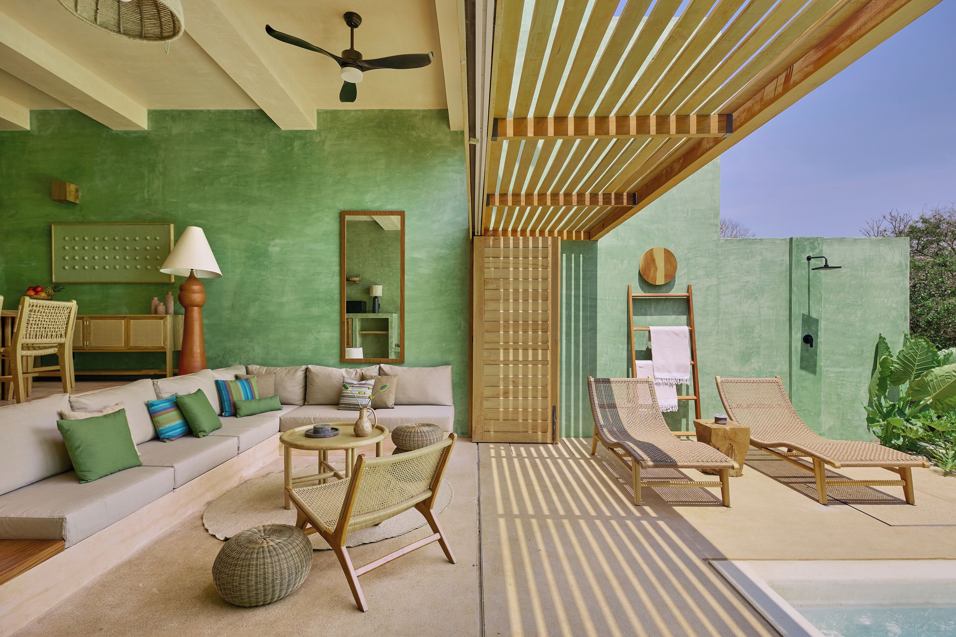 A modern living room with a green wall, a sofa with cushions, a coffee table, and a wicker chair.