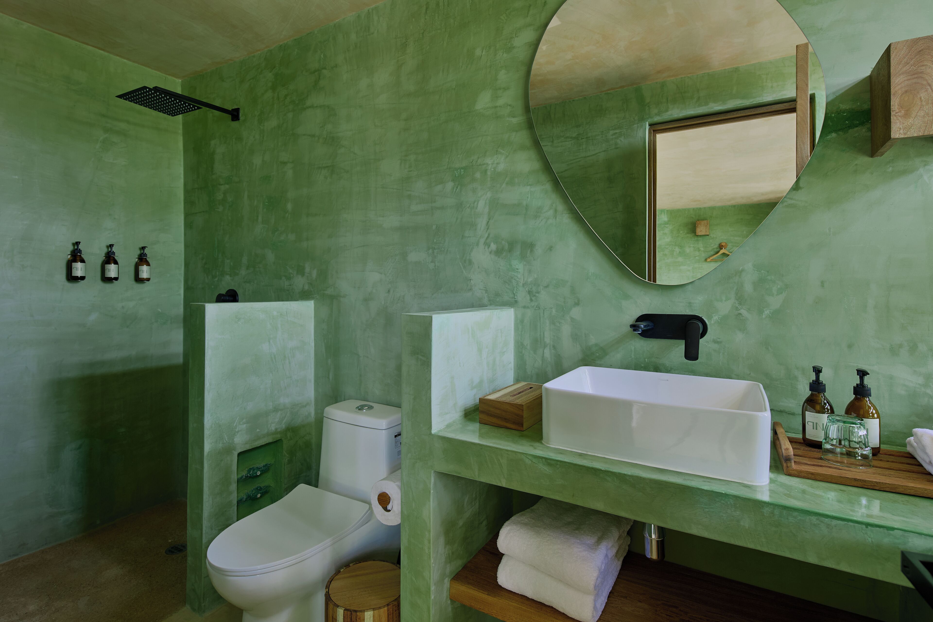 Un baño con pared verde, lavabo blanco, espejo y retrete.