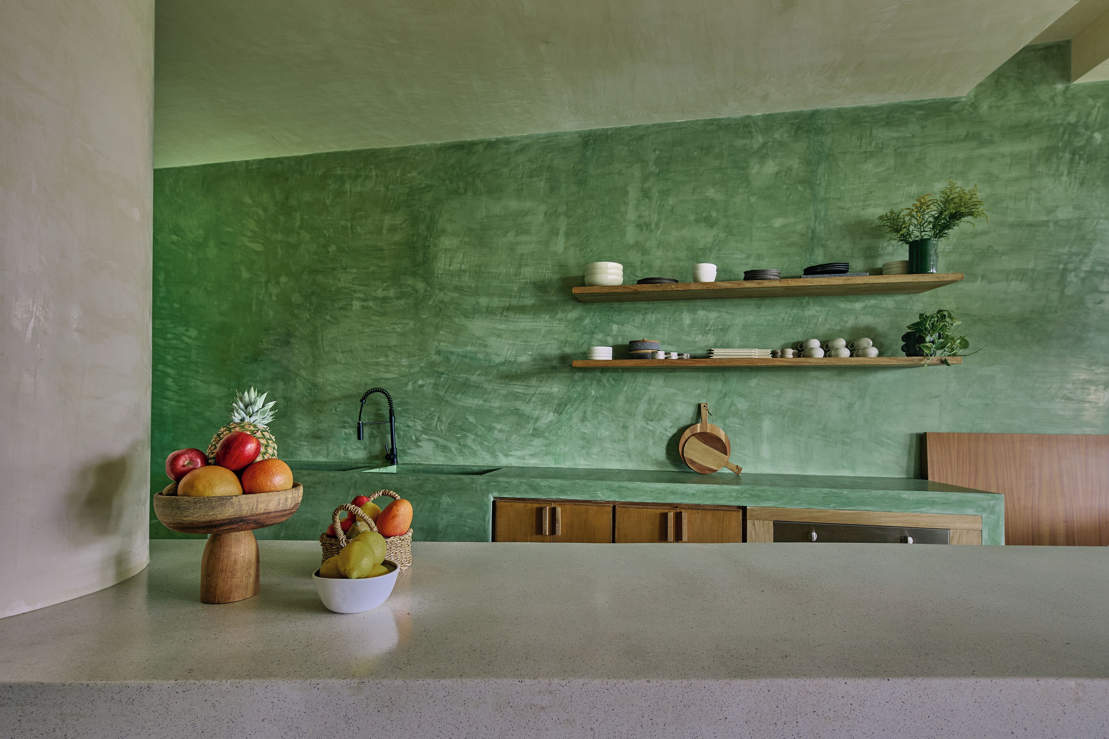 Eine Küche mit grüner Wand, Holzregalen und einer Obstschale.
