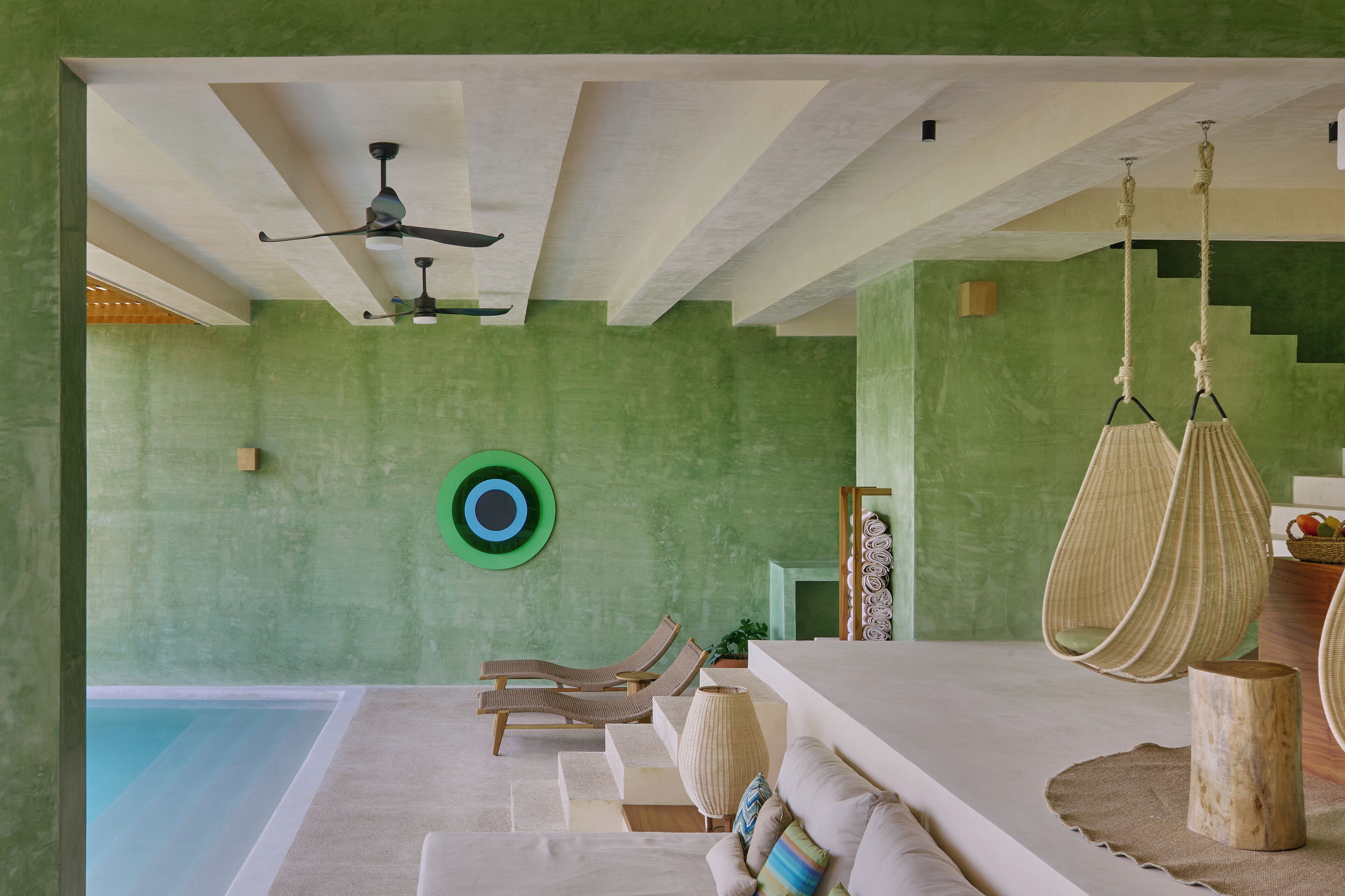 Habitación con piscina, paredes verdes, ventilador de techo y una silla colgante.