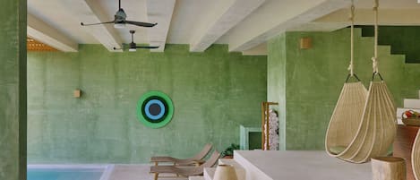 Habitación con piscina, paredes verdes, ventilador de techo y una silla colgante.