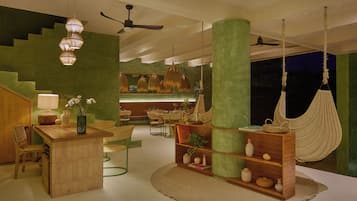 A modern interior with a wooden bar, green walls, hanging lights, a hammock, and a ceiling fan.