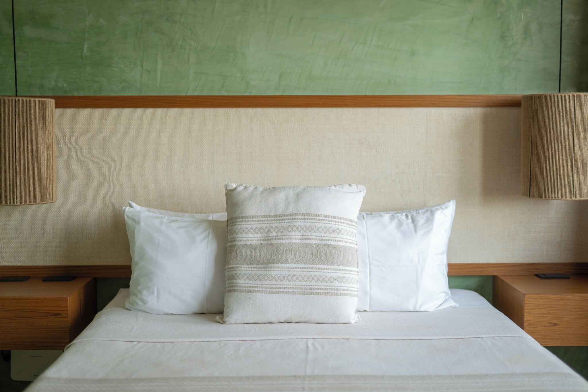 A neatly made bed with white linens and pillows, a wooden headboard, and two bedside lamps.