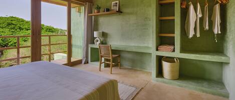 Un dormitorio con una cama grande, una silla, un estante con ropa y vistas al exterior con vegetación.