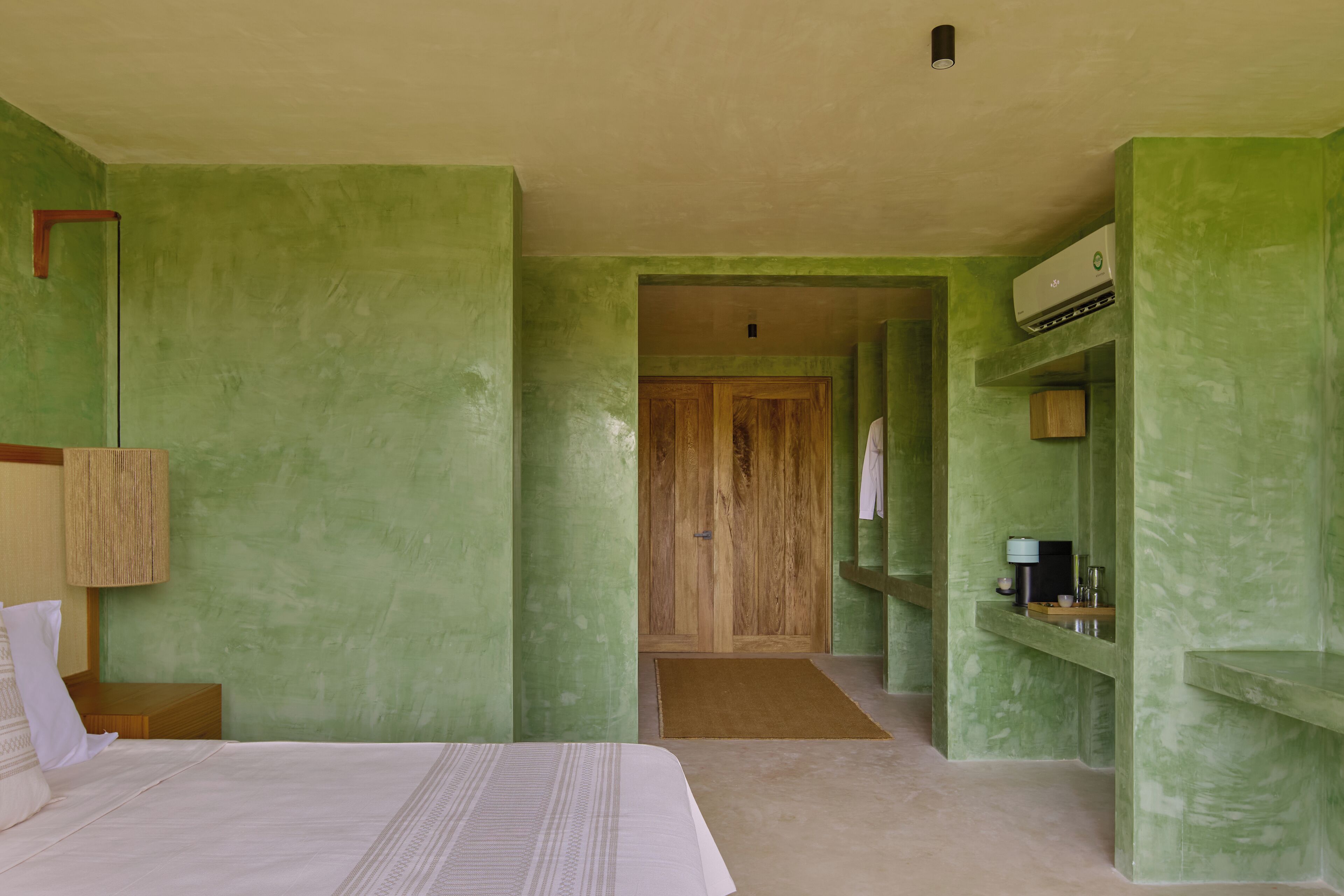 Een kamer met een bed, een houten deur, een plank met toiletartikelen en een wandairconditioning.