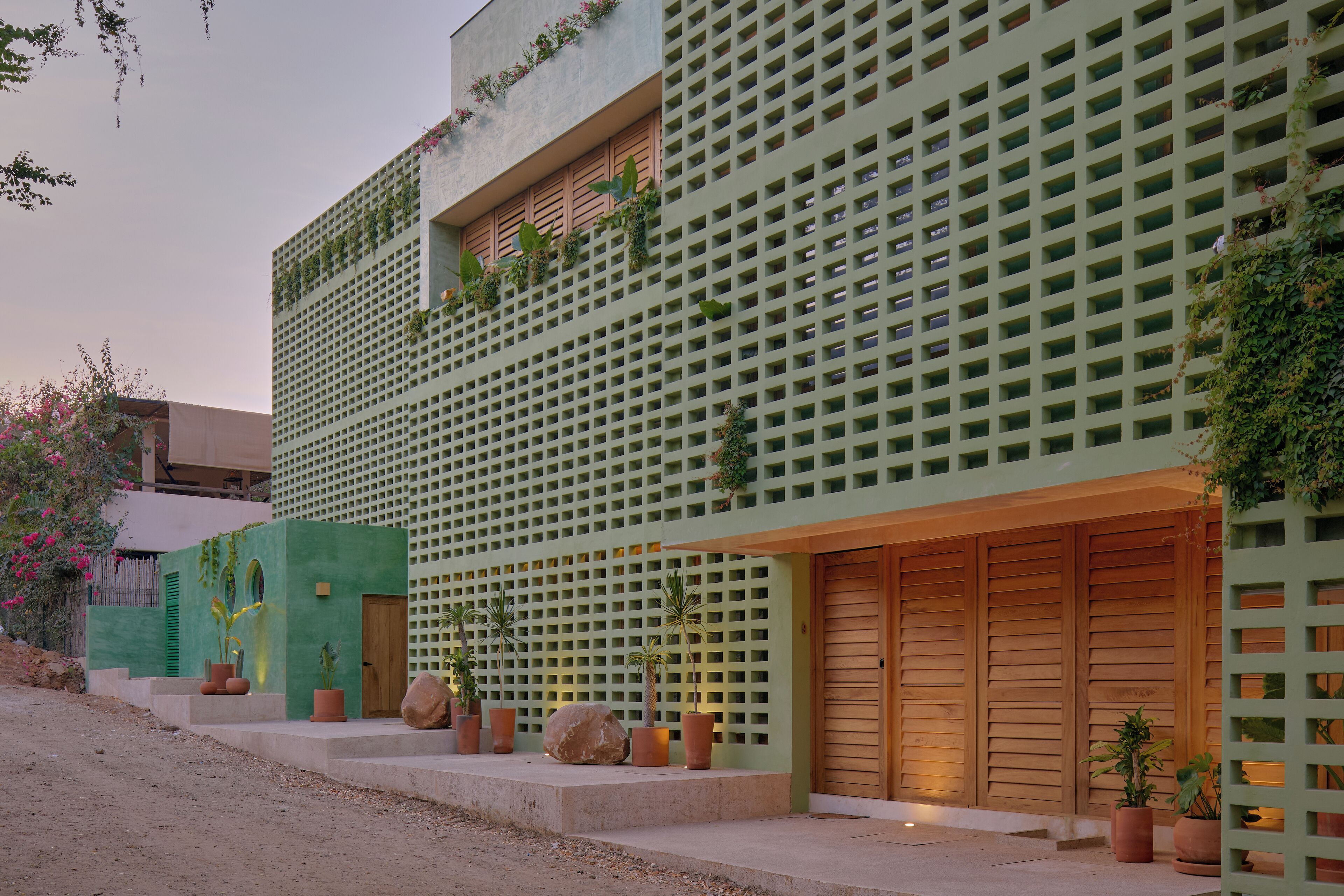 A modern building with a green facade, wooden doors, and potted plants.