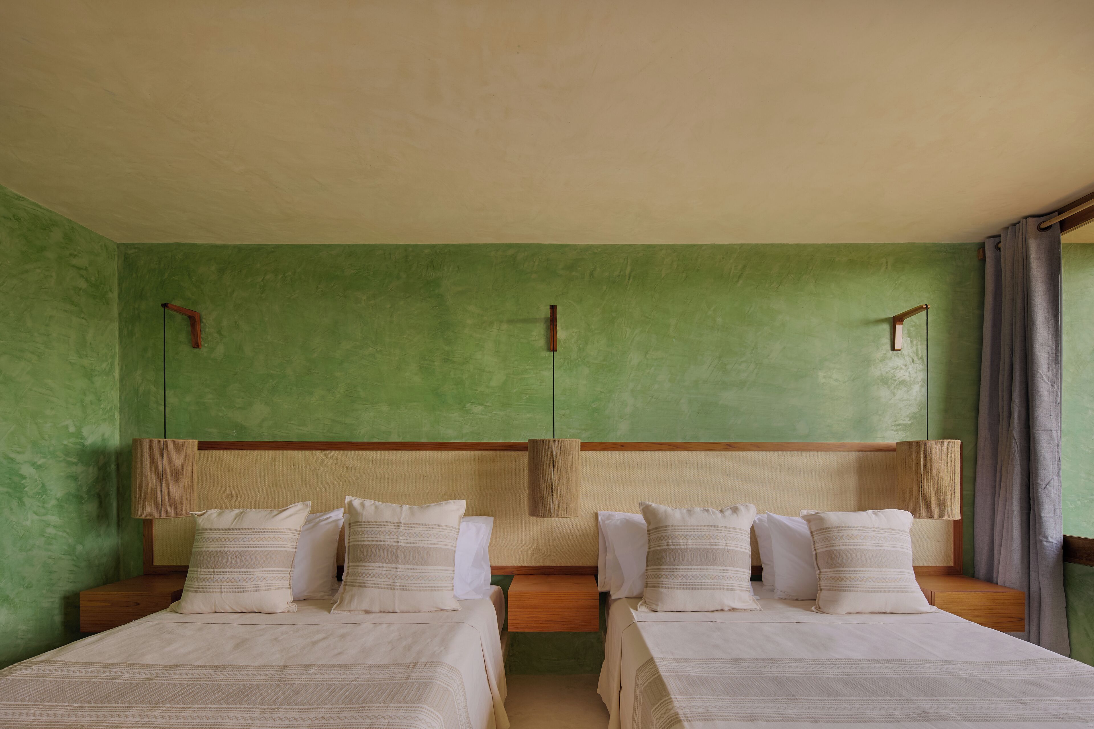 A room with two beds, green walls, wooden headboards, and bedside lamps.