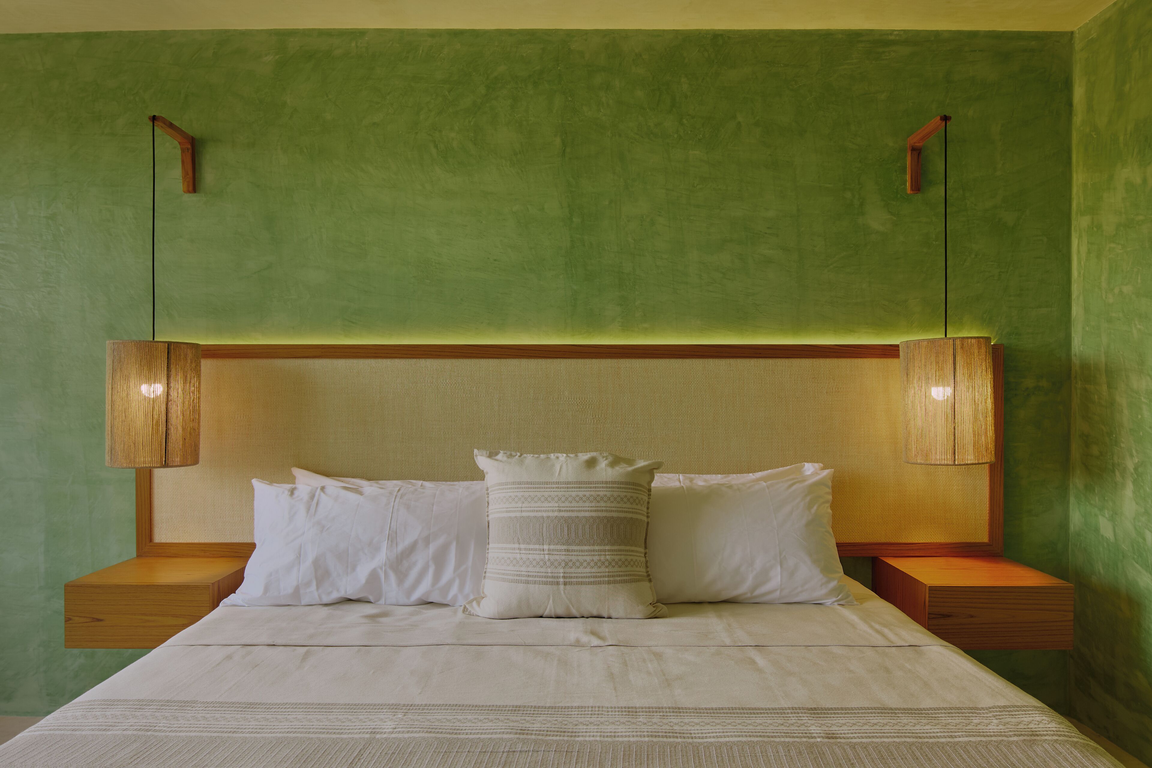 A neatly made bed with white linens and a decorative pillow, flanked by wooden nightstands and two wall-mounted lamps.