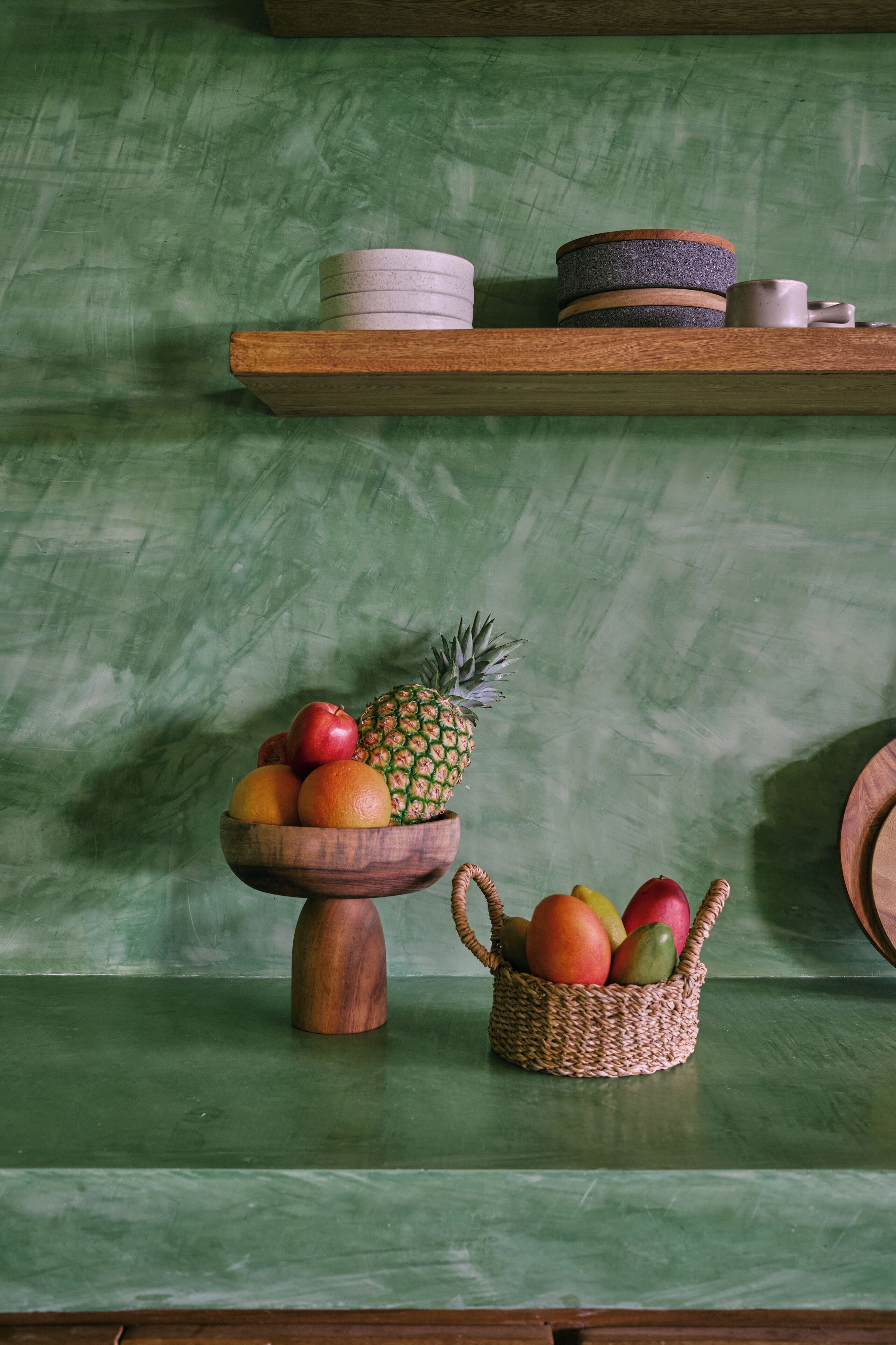 Uno scaffale di legno con ciotole e un cesto in vimini pieno di frutta.