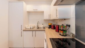 A compact kitchen with white cabinetry, a stainless steel sink, a toaster, and a range hood.