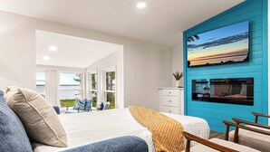 A modern bedroom with a large bed, a TV mounted on a blue wall, and a view of the outdoors. - Lakefront Modern home. Gorgeous Sunsets! near Sylvan Beach (Canastota)
