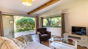 A modern living room with a sofa, armchair, and a coffee table. There is a television on a stand and a window with curtains. - 06BV2 : Nice cottage with pool (Grasse)