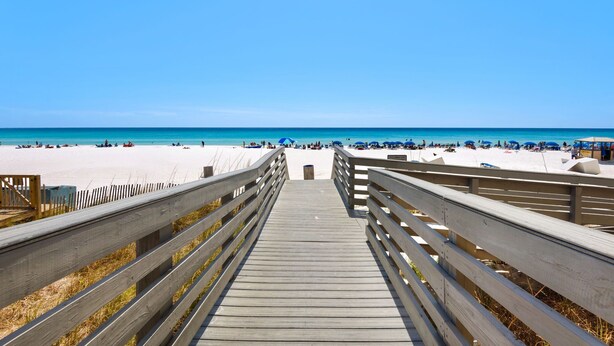Ein hölzerner Steg führt zu einem Strand unter blauem Himmel.