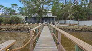 A wooden bridge leading to a house with a porch, surrounded by trees and a body of water. - 3br/3.ba With Dock, Deck/balcony and Fireplace (Santa Rosa Beach)