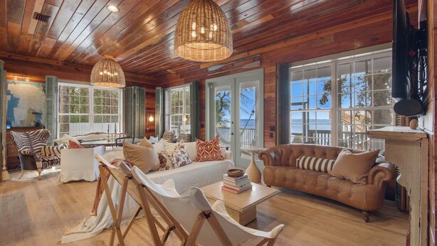 A spacious living room with a large sofa, a smaller couch, and a dining table. There are multiple windows offering views of the outdoors. - 3br/3.ba With Dock, Deck/balcony and Fireplace (Santa Rosa Beach)